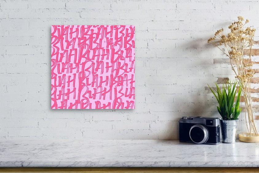 Pink abstract patterned canvas on a white brick wall with a camera and plant below.
