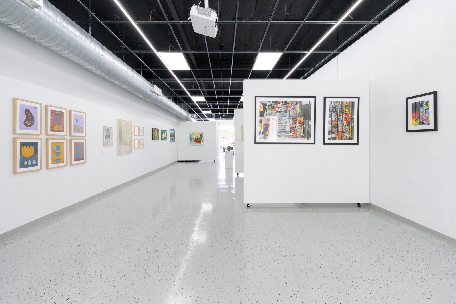 Art gallery with framed artworks on white walls and a polished floor.